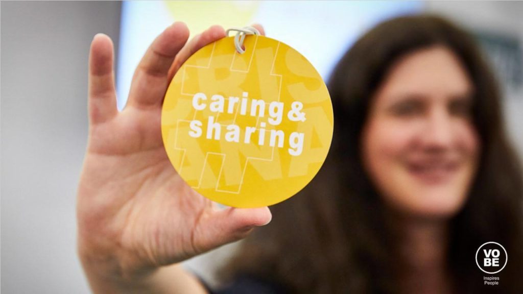 Steff Berger hält einen gelben Button mit dem Titel caring&sharing